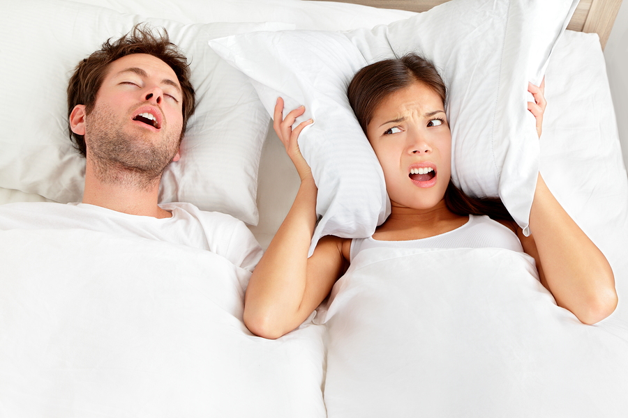 man in bed snoring next to woman holding pillow over ears. Beeville, TX sleep apnea oral appliance treatment